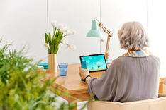 Photo of a woman from behind. She is using the GripAble device at her desk. There are white tulips on her desk.