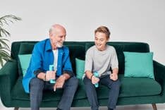 Photo of a balding man using GripAble on a green sofa besides a smiling teenage boy who is also using the Gripable device.