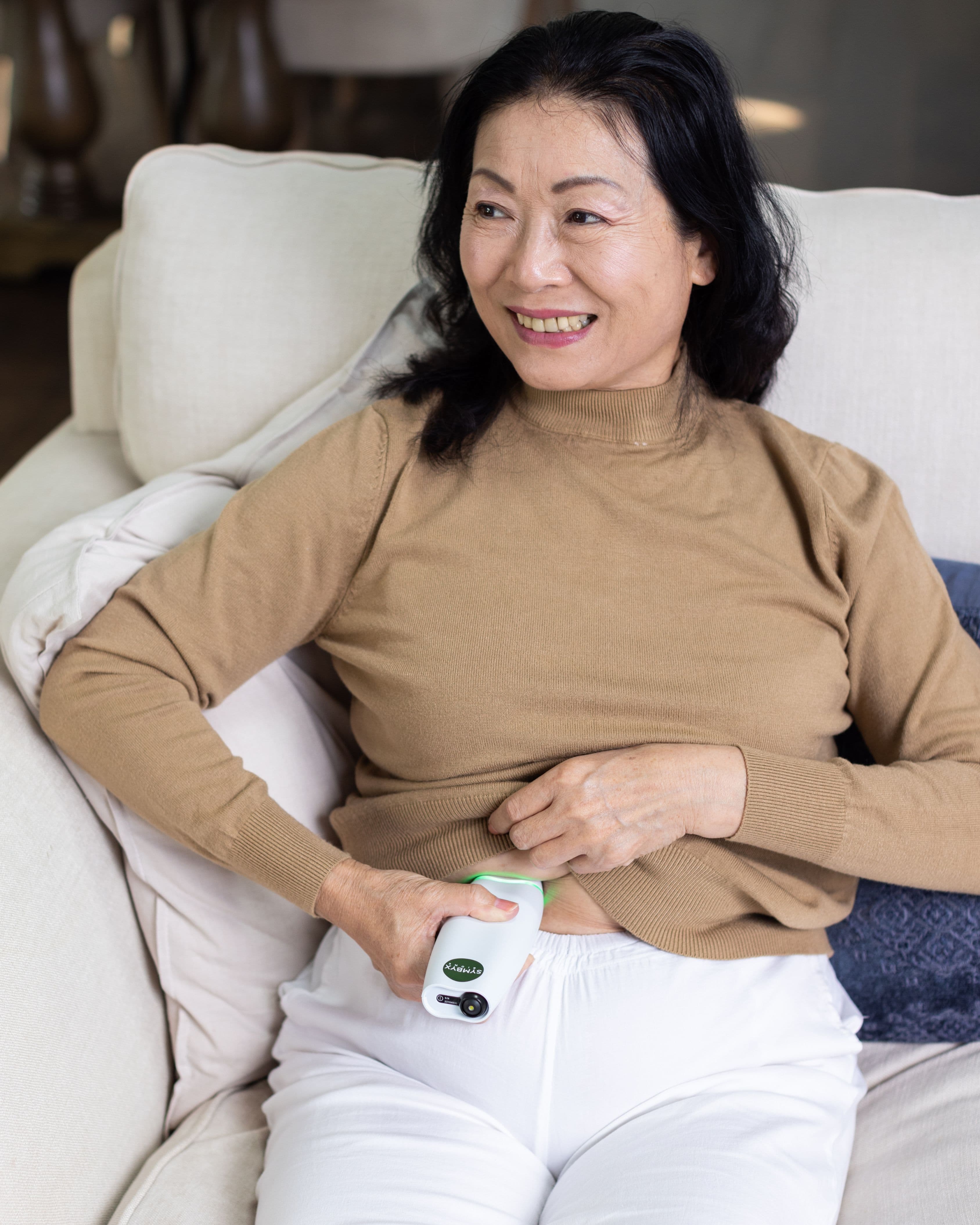 Asian woman holds a white Symbyx device to her bare stomach. Her other hand holds her jumper up.