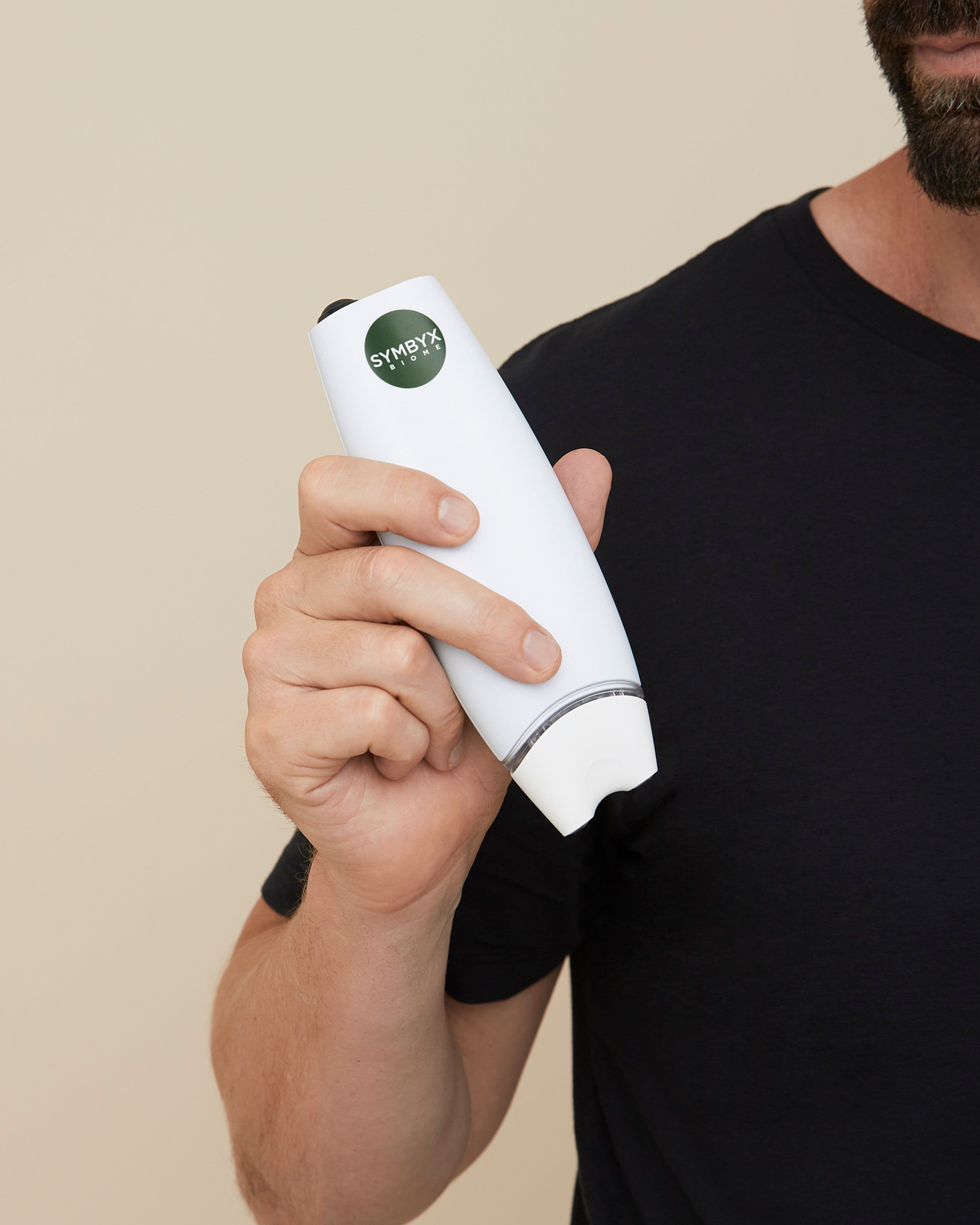 Bearded man holds a white device labelled Symbyx in one hand. He wears a black T-shirt.