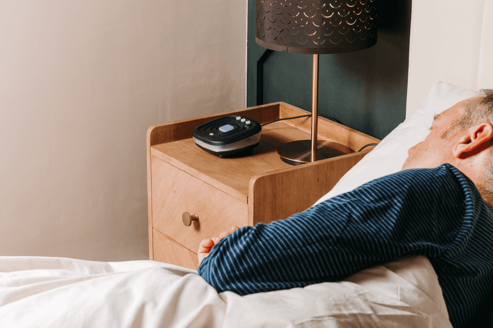 Photo of a man sleeping. The Bide device is sitting on a wooden bedside cabinet.