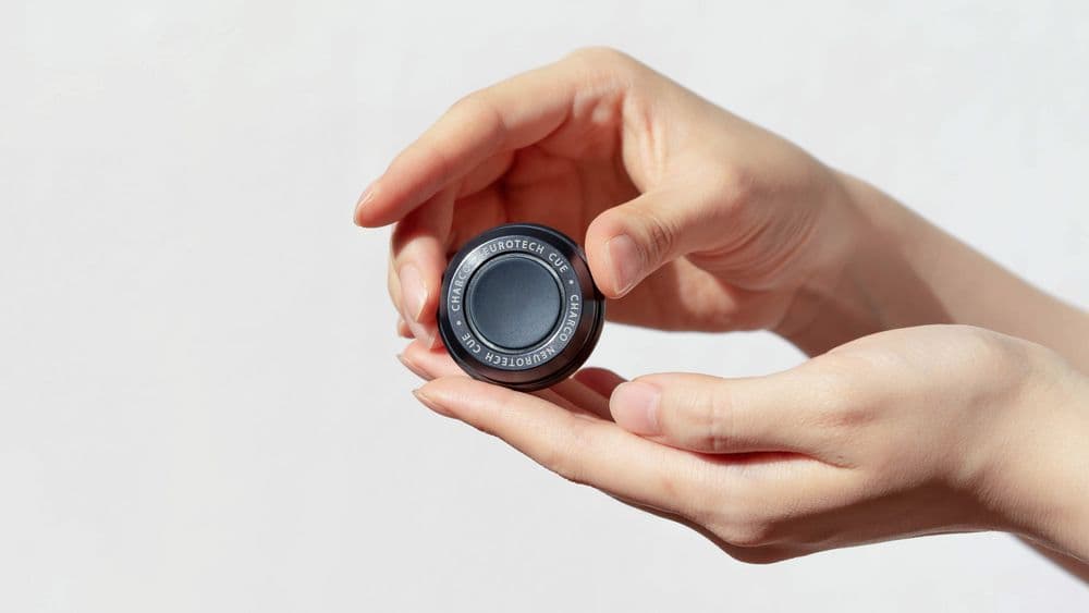 A close-up photo of a person's hand holding the CUE1+ device.