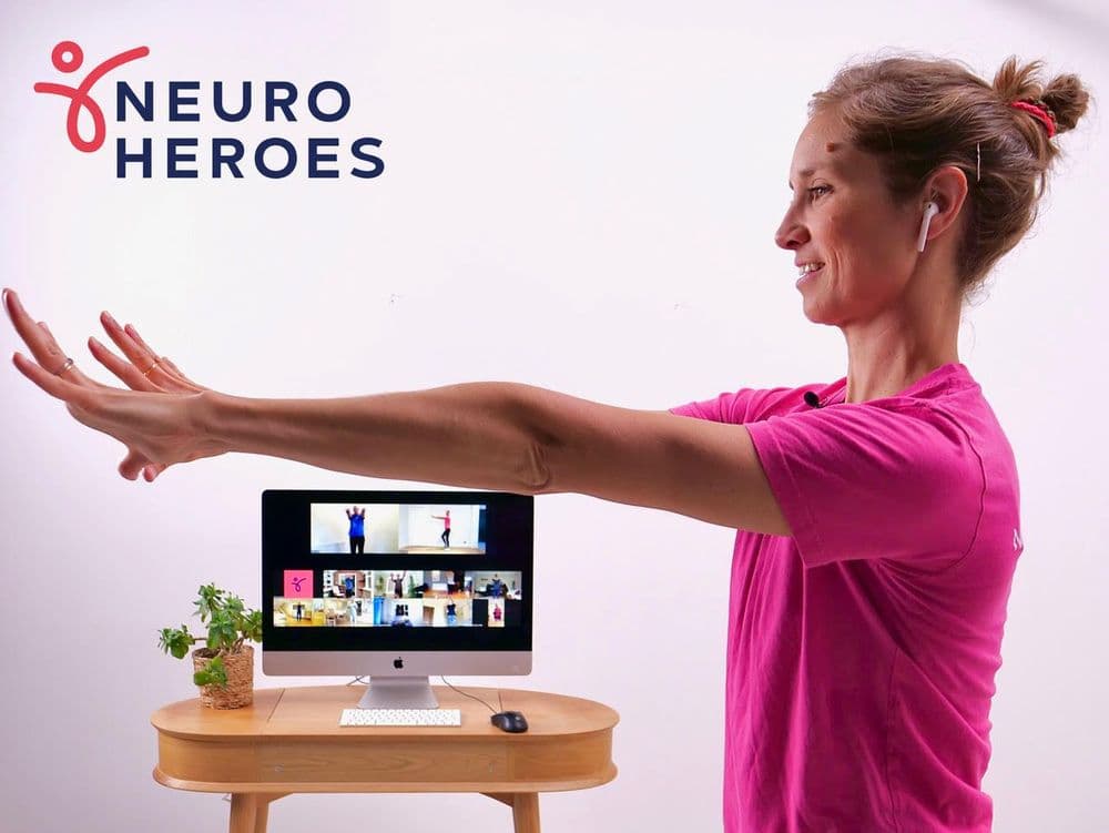 A photo of a physiotherapist conducting an online exercise class. The Neuro Heroes logo is in the top left corner.