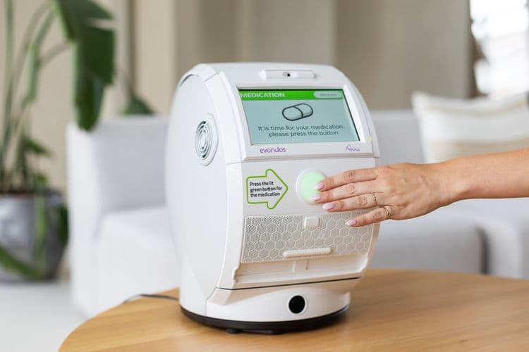 A photo of a hand reaching out to press the green button on the Evondos medicine dispenser.