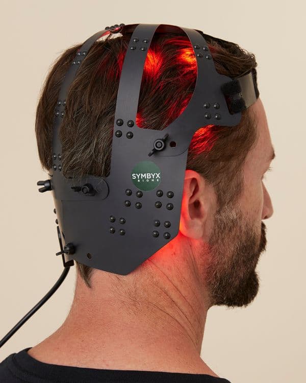 Symbyx Neuro on a white man’s head. It shines red light into his brown hair. He faces away from us.