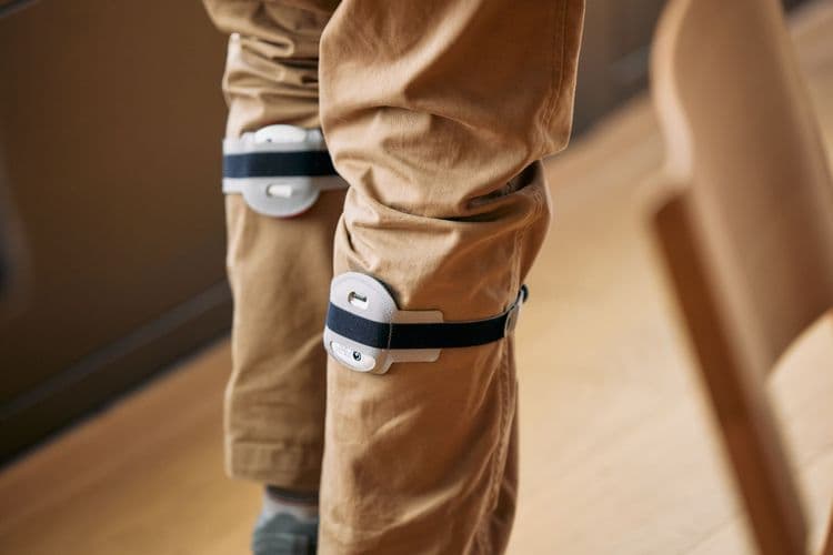 A photo of someone's legs from behind. The gaitQ Tempo are strapped around both legs over the person's trousers and just below the knees.