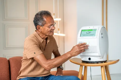 A photo of a man pressing the green lit button on his Evondos device to dispense his medication.