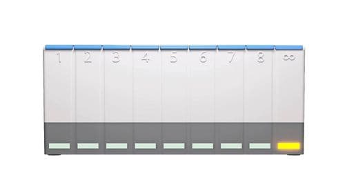 A photo of the white, grey and blue MedpeR dosette box. There is a yellowish orange light on the slot in the bottom right corner. 