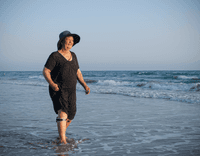 A photo of a white woman on the beach, walking along the shore while wearing the gaitq tempo on her leg.
