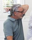 White man with grey hair holds a white Symbyx device to the back of his neck..