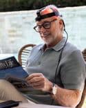 A white man with grey hair wears Symbyx Neuro while sitting in the garden reading a magazine.