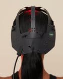 Symbyx Neuro on woman’s head. It shines red light into her long black hair. She faces away from us.