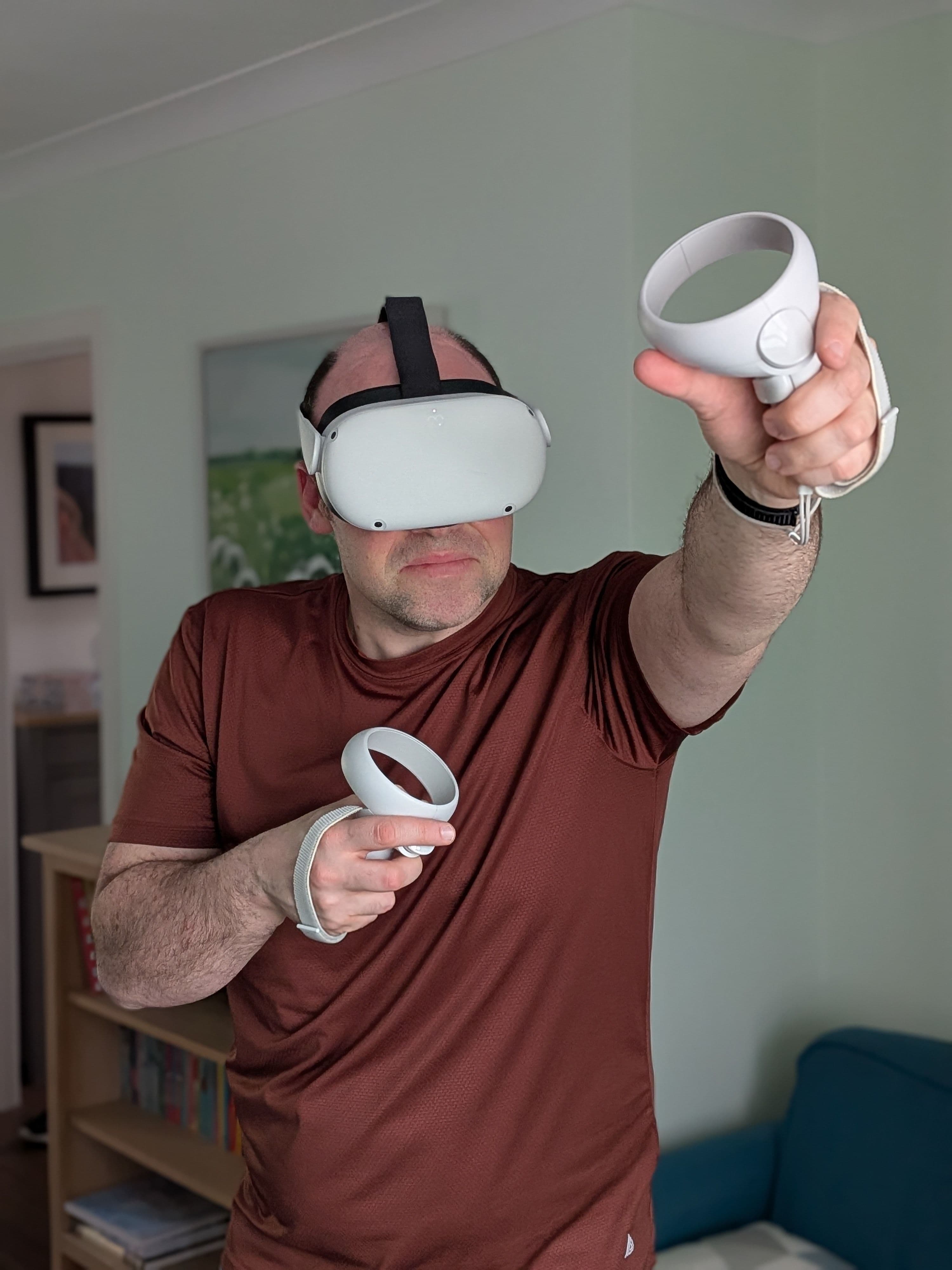 A photo of Paul Morris wearing a wear headset and holding a controller in each hand. He is reaching one arm forward in action.